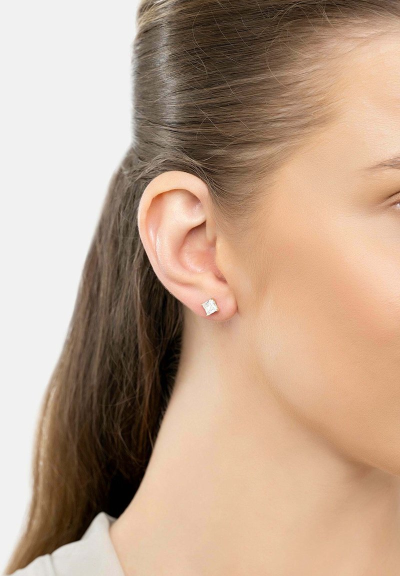 Silver stud earrings with a square, clear cubic zirconia design, showcased against a neutral background, worn on a model's ear.