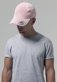Căciulă de baseball roz din suede, cu vizor curbat, având un autocolant cu logo. Purtați cu un tricou gri cu mânecă scurtă, care are o croială lejeră.
