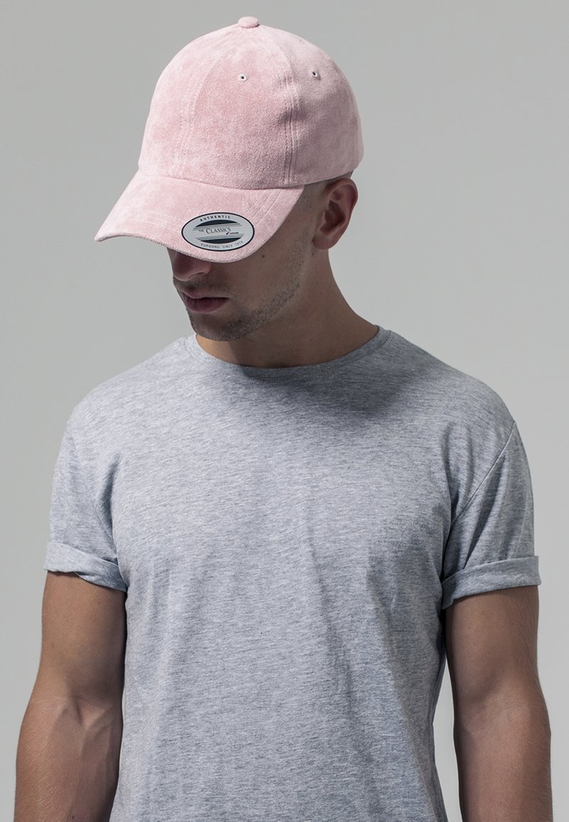 Căciulă de baseball roz din suede, cu vizor curbat, având un autocolant cu logo. Purtați cu un tricou gri cu mânecă scurtă, care are o croială lejeră.