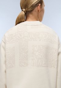 Beige sweatshirt met textuurpatronen in een lichtere tint, met een relaxed fit en een ronde hals. De achterkant toont subtiele details.