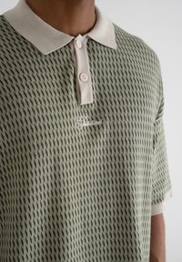 Short-sleeve polo shirt in green patterned knit, featuring a beige collar and two buttons, with an embroidered logo on the chest.