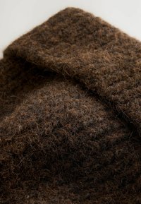 Brunt tekstureret stof med et fuzzy, strikket udseende i forskellige nuancer af brunt og tynde, løse fibre. Blødt og varmt materiale.
