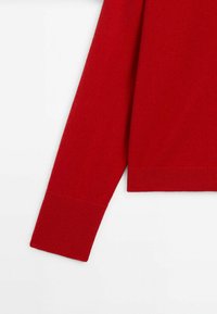 Punainen neulottu villapaita, jonka hiha on ribbatulla reunuksella. Kangas näyttää pehmeältä, sillä siinä on sileä tekstuuri eikä näkyviä kuvioita.