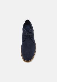 Pantofii din suede bleu marin au un superior texturat, vârful rotund și o talpă din cauciuc marron. Dispune de două orificii pentru șireturi și un design minimalistic.