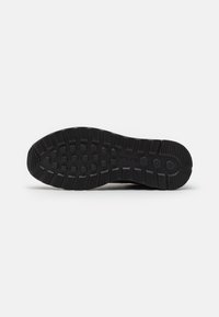 Semelle de chaussure en caoutchouc noir avec des crampons circulaires et rectangulaires et un bord texturé pour une meilleure adhérence, vue de dessous.
