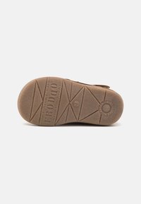 Suela de zapato de goma marrón con una superficie texturizada y flexible, un patrón de dibujo geométrico y el nombre de la marca "FRODDO" en relieve.