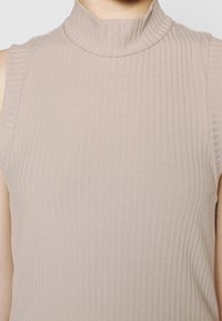 Top senza maniche con collo alto in morbido tessuto beige chiaro a costine, caratterizzato da una texture liscia e una leggera elasticità. Design aderente che mette in risalto la silhouette.