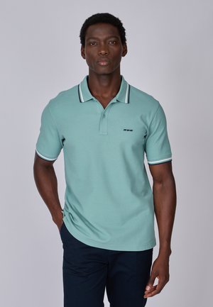 Polo vert pâle en tissu doux avec une patte de boutonnage à trois boutons, un col rayé bleu marine et blanc, et un logo brodé sur la poitrine.