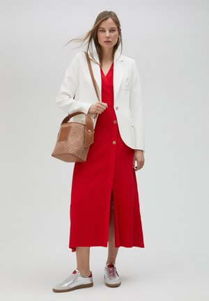 Vestido midi rojo con canalé y abertura frontal, combinado con un blazer blanco. Los accesorios incluyen un bolso marrón con estampado y zapatillas plateadas.