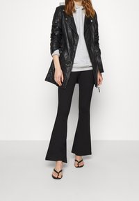 Czarna skórzana kurtka motocyklowa z srebrnymi detalami, noszona na jasnoszarym hoodie. Czarna spódnica w kształcie dzwonów i czarne klapki dopełniają stylizację.