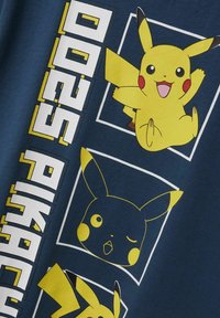 Navy blue kangas dengan grafis Pikachu kuning; menampilkan beberapa ilustrasi, termasuk Pikachu yang tersenyum dan berkedip, serta teks yang tebal.