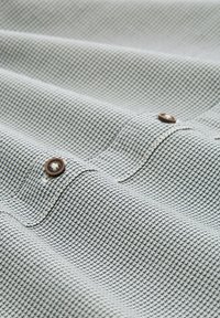 Primo piano di un tessuto grigio chiaro piegato, con una texture e un piccolo motivo geometrico nero, e bottoni marroni.