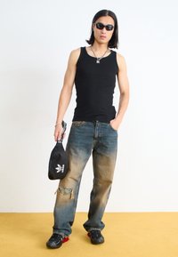 Black tank top, faded blue jeans with ripped detail, black sneakers with red accents, and an Adidas bag in hand, set against a plain background.