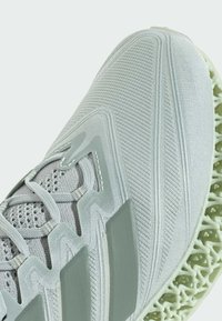 Lichtgrijs sportshoe met een textuur van gaas aan de bovenkant en een groene 3D-geprinte zool. Heeft overlay-accenten en een vetersluiting ontwerp.