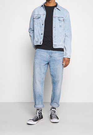 Lyseblå denimjakke med to brystlommer, kombineret med en sort t-shirt, lyseblå jeans med optrukne buksekanter og sorte høje sneakers.