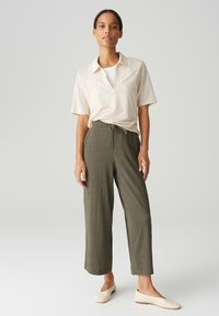 Chemise beige clair à manches courtes et col, associée à un pantalon large texturé vert olive. Portée avec des ballerines couleur crème.