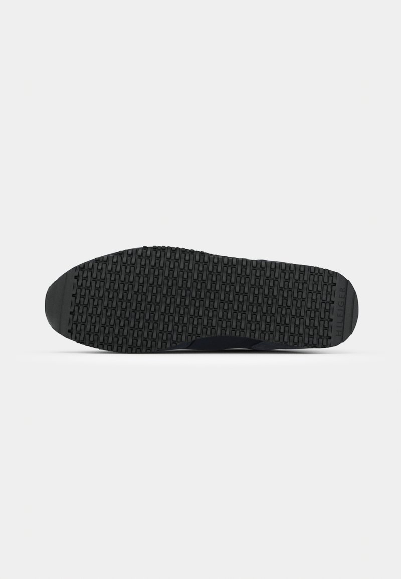 Semelle en caoutchouc noir avec un motif rectangulaire texturé et répétitif, et le mot "HILFIGER" embossé au niveau du talon droit.