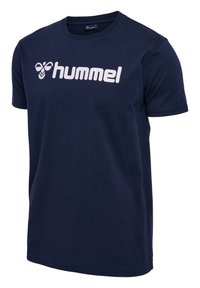 Camiseta de algodón de color azul marino con mangas cortas, que presenta un gran logo en blanco de "hummel" en la parte delantera. Textura suave y escote de estilo clásico.