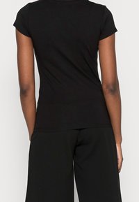 Camiseta negra de manga corta, diseño ajustado, material de algodón suave, textura lisa, con escote redondo y detalles mínimos en el dobladillo.