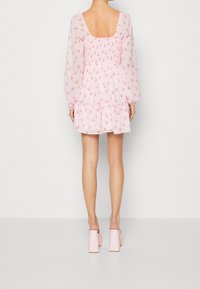 Vestido floral rosa con corsé fruncido y mangas largas. Falda acampanada que termina a la mitad del muslo, combinada con mules de tacón bloque en rosa claro.