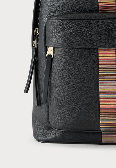 Gros plan d'une poche de sac à dos en cuir noir texturé avec des tirettes de fermeture éclair et un accent vertical rayé multicolore.