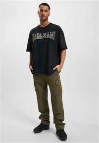 Black oversized t-shirt with white print and olive green cargo pants featuring side pockets, paired with black sneakers.