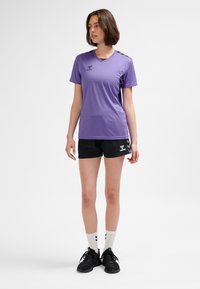 Lila sport-T-shirt med v-ringning och svarta detaljer, kombinerad med svarta shorts med en logotyp. Inkluderar vita sportstrumpor och svarta skor.