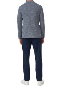 Dunkelblazer mit Struktur und einem Schlitzt, kombiniert mit dunklen Hosen. Das Ensemble wird durch weiße Sneakers abgerundet.