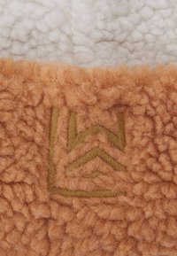 Textúrovaná tkanina v bielych a oranžových tónoch. Biely fleece vrchnák, oranžová huňatá spodná časť s vyšívaným logom v zelených tónoch.