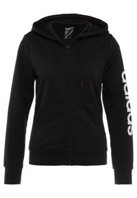 Sweat à capuche noir zippé avec poches frontales, capuche avec cordon de serrage et logo Adidas blanc vertical sur la manche gauche.