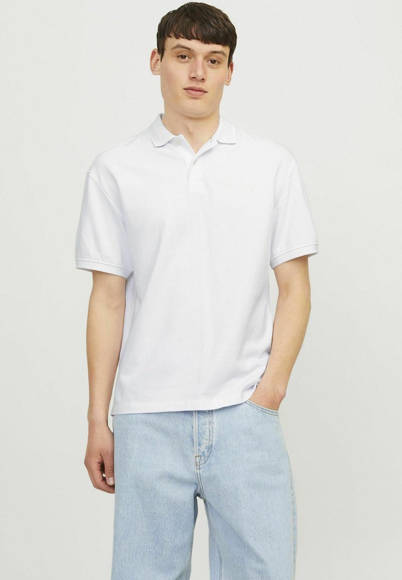 Polo alb din bumbac, cu o textură moale, mâneci scurte și un guler clasic, asociat cu pantaloni din denim albastru deschis.