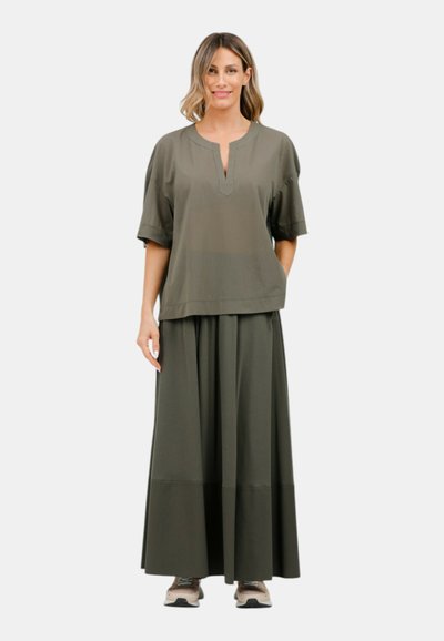 Outfit verde oliva composto da una blusa corta a maniche corte con collo a taglio e una lunga gonna fluida con una leggera piegatura.