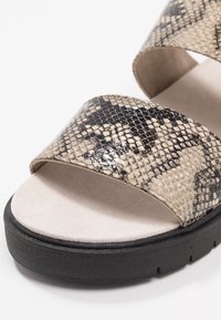 Beige ja musta käärmeprindi sandaalid, millel on kaks laia rihma, pehme tallaga ja musta kummitald. Omab siledat tekstuuri ja ümarat kuju.