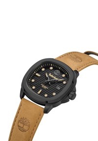 Orologio Timberland con cassa quadrata nera, cinturino in pelle beige, quadrante nero texture, indicatori delle ore dorati e display della data.