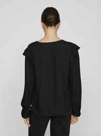 Crna bluzica dugih rukava s naboranim ramenima, okruglim izrezom i teksturiranim materijalom, s ležernim krojem.