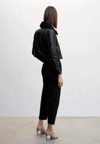 Czarna skórzana krótka kurtka z kołnierzem z baranka, w połączeniu z czarnymi zwężanymi jeansami i sandałami na metalicznym obcasie. Gładka tekstura i dopasowany krój.
