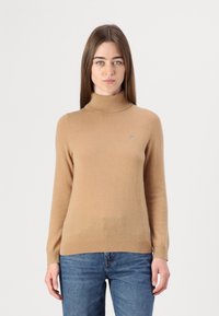 Heled pruun leelot-sweater, mis on valmistatud pehmest kangast, sobiv disain ja väike logo detail rinnal. Kantakse siniste teksadega.