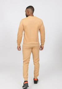 Sweat-shirt beige et jogging tapered, tous deux en tissu doux avec des poignets et une taille côtelés, assortis à des chaussures noires et orange.
