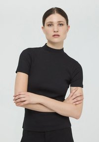 Czarna, prążkowana bluzka z krótkim rękawem o wysokim dekolcie, z dopasowanym krojem i gładką teksturą. Bez widocznych logo ani wzorów.