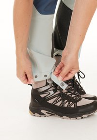 Lichtblauwe wandelschoenen met drukknoopsluitingen bij de enkels, gecombineerd met zwarte en grijze wandellaarzen met gestructureerde zolen en veters, op een witte achtergrond.
