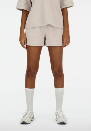 Camisa oversize beige combinada con pantalones cortos beige a juego. Medias blancas texturizadas hasta la rodilla y zapatillas ligeras complementan el atuendo.