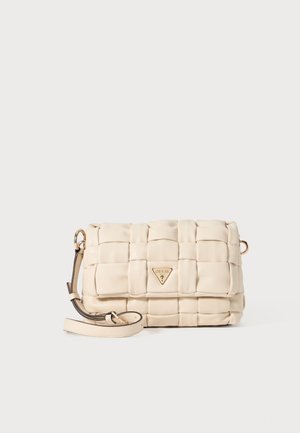 Sac en bandoulière beige matelassé avec un emblème doré et une bandoulière amovible. Fabriqué dans un matériau lisse avec une forme rectangulaire.