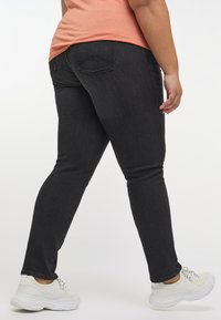 Svarta smala jeans med en slät yta, medelhög midja och bakfickor. Matchas med kraftiga vita sneakers.