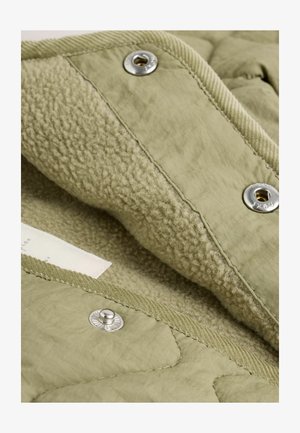 Oliivroheline tikitud jakki siseosa pehme fliisvoodriga, hõbedased nööbid ja ribatud aktsendid servadel. Tekstuuriga kangas on nähtav.