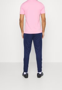 T-shirt rosa a maniche corte abbinato a pantaloni sportivi blu marino, con una texture liscia e una vestibilità comoda. Scarpe da ginnastica nere completano il look.