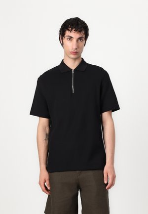 Black short-sleeve polo shirt with a zippered collar, made of a smooth fabric. The fit is relaxed, and the design is simple and minimalistic.