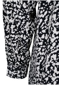 Chemise boutonnée noire et blanche avec un motif éclaboussé, dotée d'un tissu texturé et d'un détail de poignets avec deux boutons noirs.