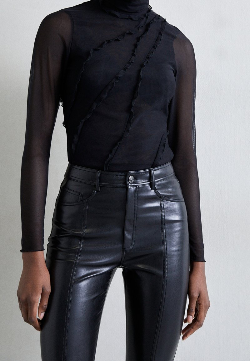 Svart långärmad topp med volangdetaljer och hög krage, i kombination med högmidjade svarta fodrade läderbyxor med framfickor.
