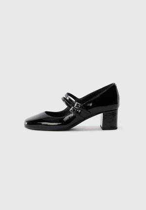 Scarpa Mary Jane in pelle verniciata nera con due cinturini a fibbia e tacco basso su sfondo bianco.