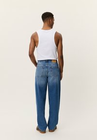 Ανοιχτό μπλε, τζιν παντελόνι με ψηλή μέση και ξεθωριασμένο φινίρισμα, δύο τσέπες στην πλάτη και καφέ δερμάτινο ταμπελάκι στη μέση. Συνδυάζεται με λευκό αμάνικο τοπ.